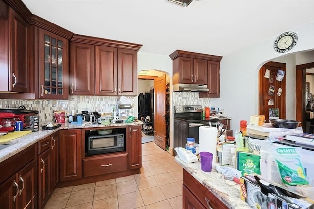 kitchen with black microwave, under cabinet range hood, light tile patterned floors, stainless steel electric range, and arched walkways