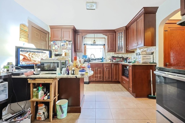 kitchen with tasteful backsplash, arched walkways, appliances with stainless steel finishes, light tile patterned flooring, and glass insert cabinets