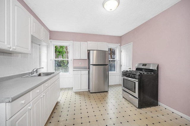 kitchen with appliances with stainless steel finishes, a sink, white cabinetry, and tasteful backsplash
