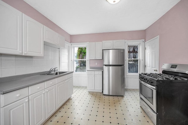kitchen featuring appliances with stainless steel finishes, a sink, white cabinets, decorative backsplash, and light floors