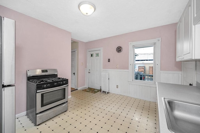 kitchen with stainless steel range with gas cooktop, wainscoting, freestanding refrigerator, a sink, and white cabinetry