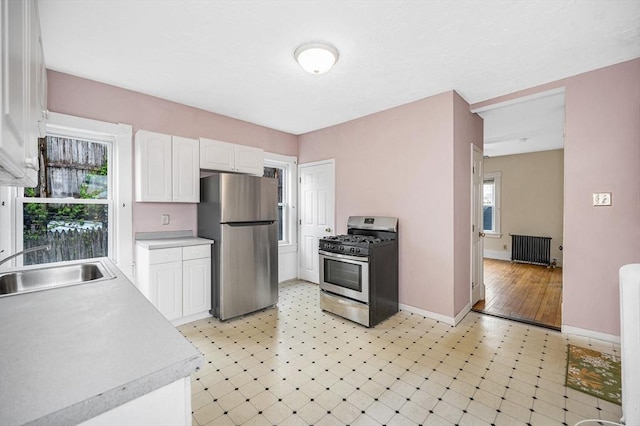 kitchen featuring stainless steel appliances, radiator heating unit, white cabinetry, a sink, and light countertops
