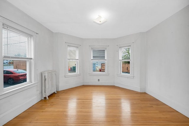 spare room featuring radiator heating unit, light wood-style flooring, and baseboards
