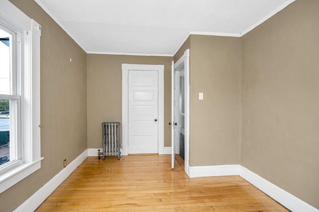 spare room with radiator, light wood-style floors, baseboards, and crown molding