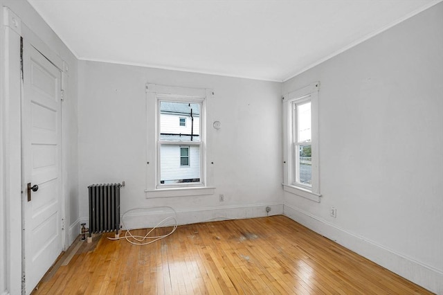 unfurnished room featuring radiator, light wood-type flooring, ornamental molding, and baseboards