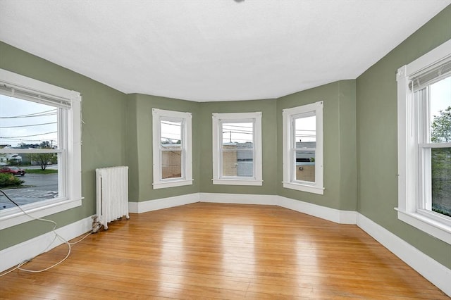 unfurnished room featuring radiator heating unit, light wood finished floors, plenty of natural light, and baseboards