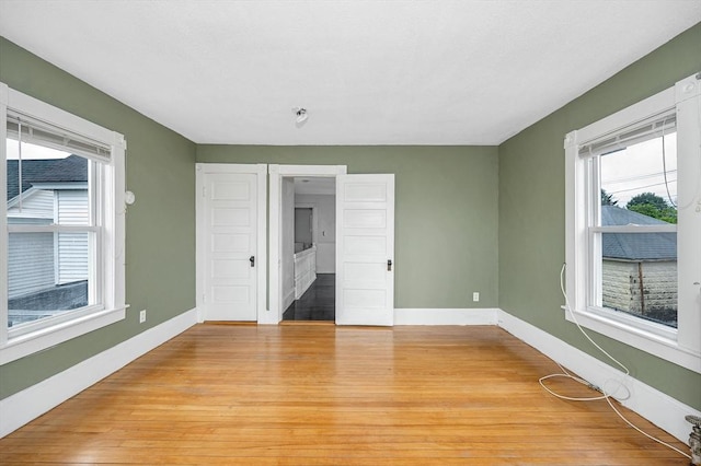 unfurnished bedroom featuring multiple windows, light wood-type flooring, and baseboards