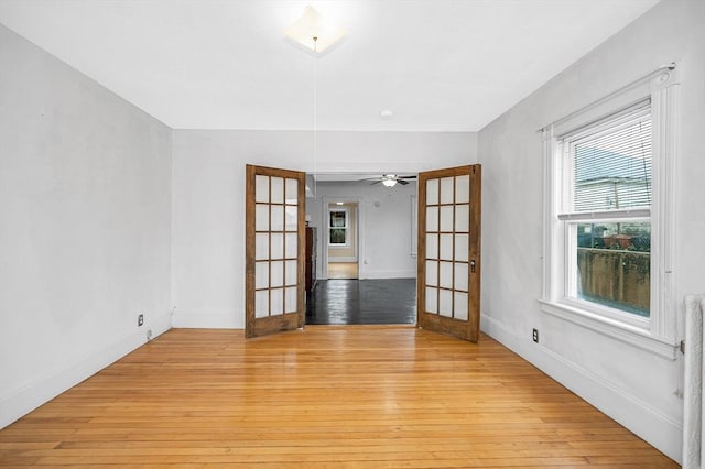 empty room with french doors, light wood finished floors, and baseboards