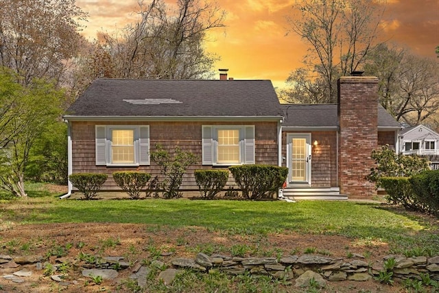 view of front of home with roof with shingles, a chimney, and a front yard
