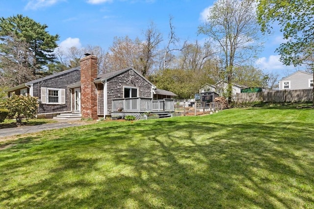 exterior space featuring fence, a wooden deck, a chimney, and a lawn