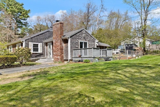 rear view of property featuring a chimney, a yard, and a deck