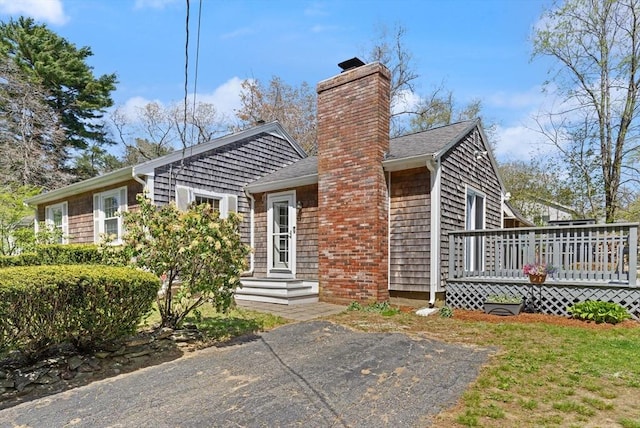 view of front of property featuring a deck, a chimney, and a shingled roof