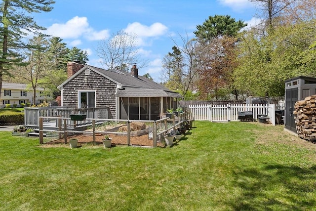 rear view of house with a lawn, a chimney, a fenced backyard, and a sunroom