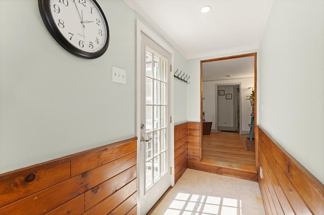 corridor with ornamental molding, wooden walls, a wainscoted wall, and a healthy amount of sunlight