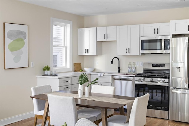 kitchen featuring white cabinets, light wood-style floors, stainless steel appliances, and light countertops