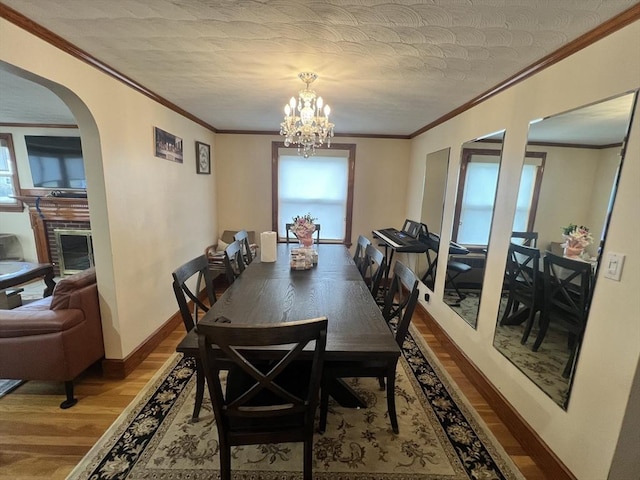 dining space with a chandelier, wood finished floors, baseboards, ornamental molding, and a glass covered fireplace