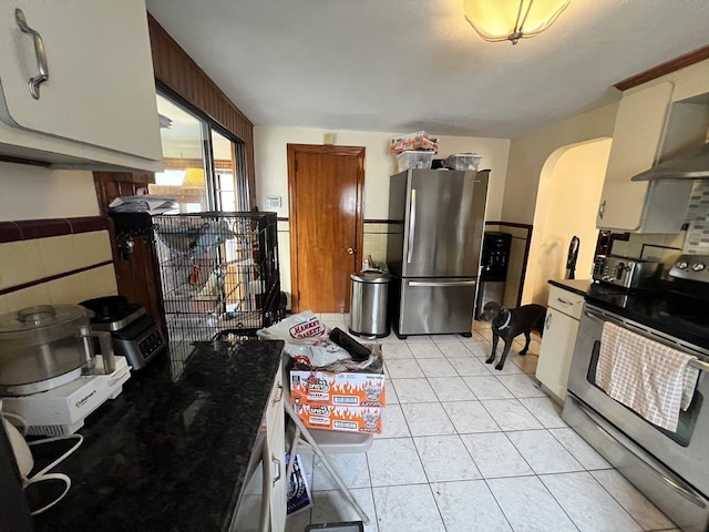 kitchen with light tile patterned floors, arched walkways, wainscoting, dark countertops, and stainless steel appliances