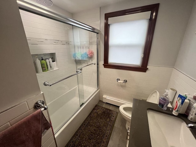 full bath featuring toilet, a wainscoted wall, shower / bath combination with glass door, a sink, and tile walls