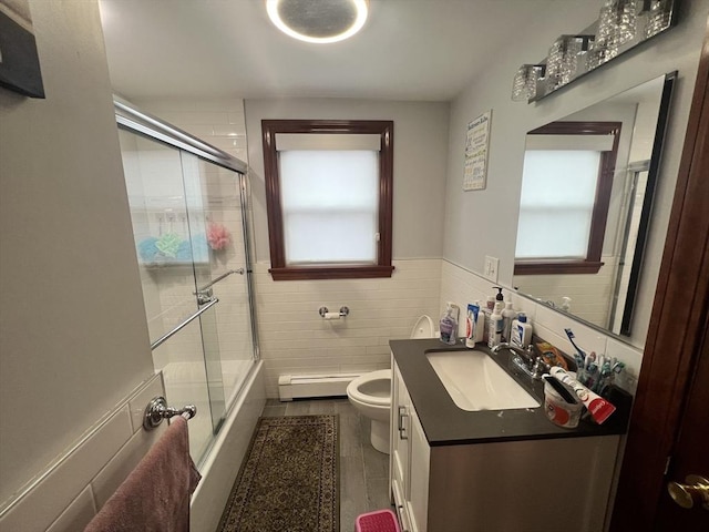 bathroom with a baseboard heating unit, a wainscoted wall, toilet, and a healthy amount of sunlight