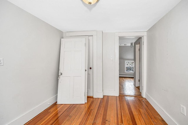 unfurnished bedroom featuring a closet, hardwood / wood-style flooring, and baseboard heating