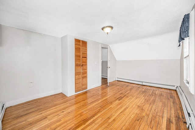 additional living space featuring light hardwood / wood-style floors, a baseboard radiator, and vaulted ceiling