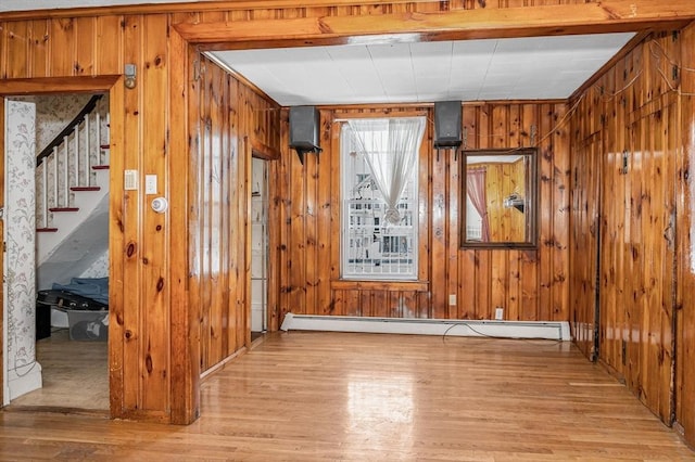 interior space with a baseboard heating unit, light hardwood / wood-style flooring, and wooden walls