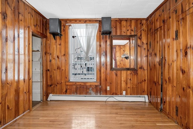 spare room with light wood-type flooring, wood walls, and baseboard heating