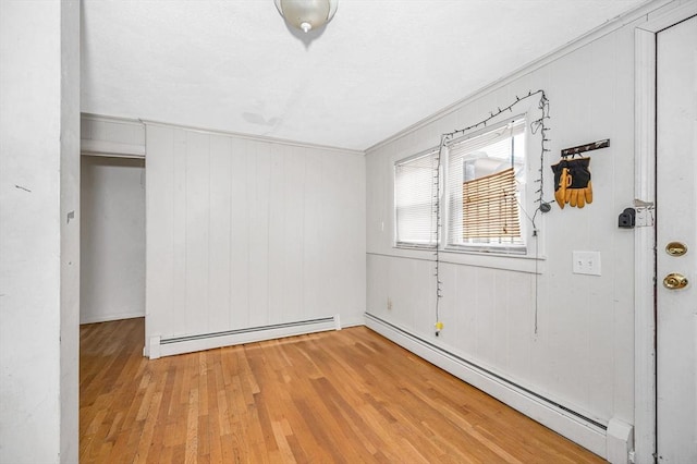 empty room with baseboard heating, light hardwood / wood-style flooring, ornamental molding, and wooden walls