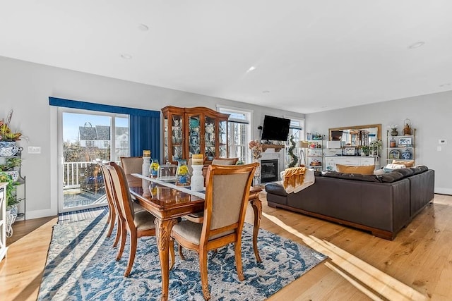 dining area featuring light wood finished floors, baseboards, and a glass covered fireplace