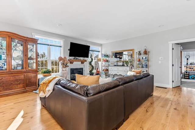 living area with light wood-type flooring, baseboards, and a glass covered fireplace