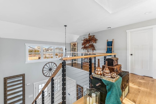 hallway with vaulted ceiling, hardwood / wood-style floors, visible vents, and an upstairs landing
