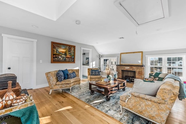 living room with lofted ceiling, visible vents, attic access, a stone fireplace, and wood finished floors