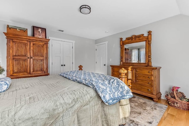 bedroom featuring a closet, visible vents, vaulted ceiling, and wood finished floors