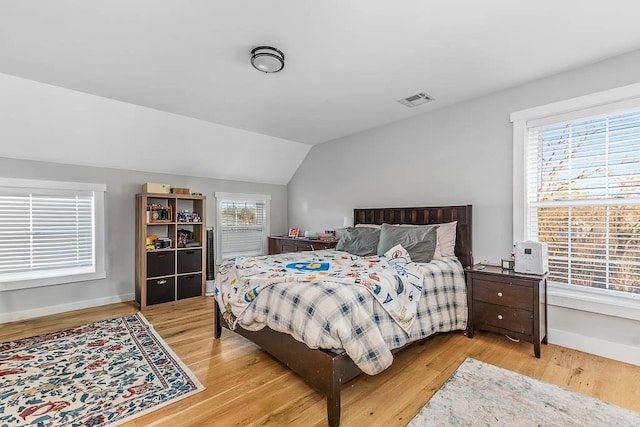 bedroom with light wood-style floors, lofted ceiling, visible vents, and baseboards