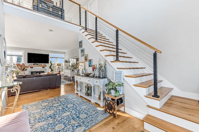 stairs with a fireplace, wood finished floors, and a towering ceiling