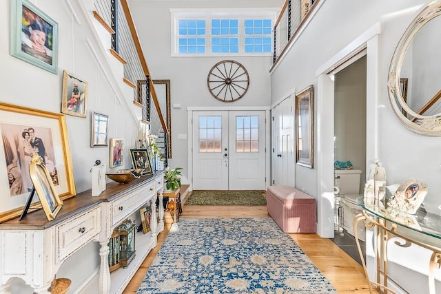 entrance foyer featuring light wood-style flooring, a high ceiling, stairway, and french doors