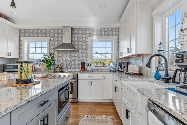 kitchen with stainless steel appliances, wall chimney range hood, a wealth of natural light, and white cabinets