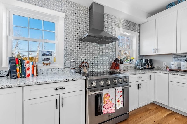 kitchen featuring white cabinetry, wall chimney range hood, light wood-type flooring, backsplash, and high end range