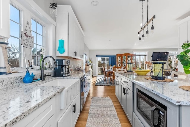 kitchen featuring white cabinets, light wood-style flooring, light stone countertops, stainless steel dishwasher, and a sink