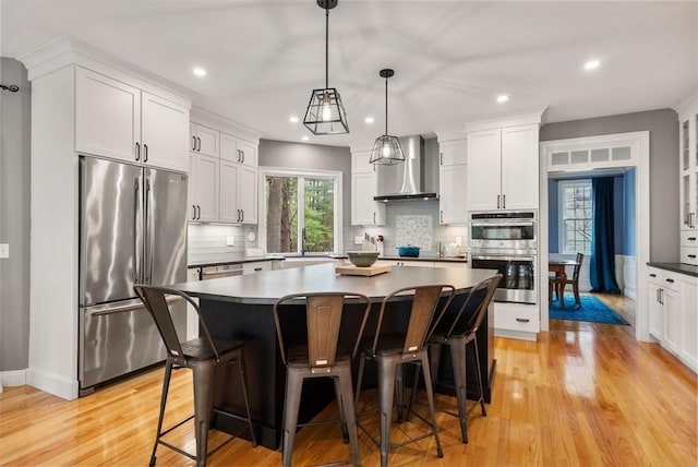 kitchen with stainless steel appliances, light wood-type flooring, wall chimney exhaust hood, and a breakfast bar area