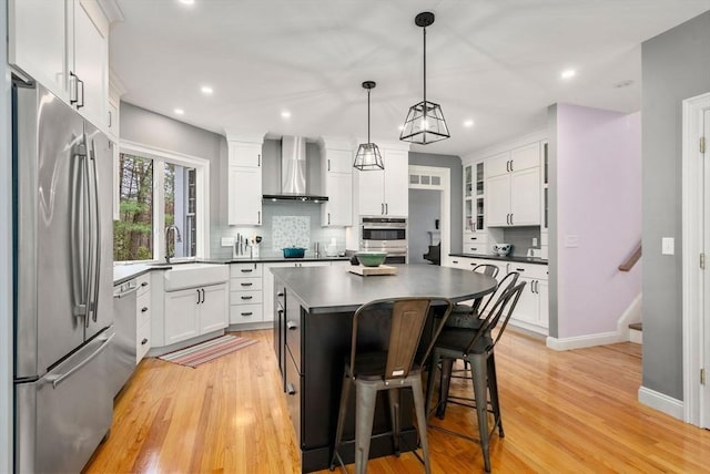 kitchen featuring light wood-type flooring, wall chimney range hood, dark countertops, a sink, and stainless steel appliances