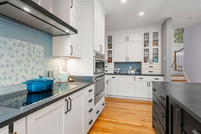 kitchen featuring wall chimney exhaust hood, glass insert cabinets, white cabinetry, dark countertops, and black electric stovetop