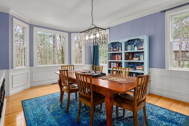 dining area with light wood-style flooring, a notable chandelier, ornamental molding, and a wainscoted wall