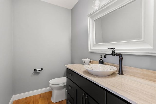 half bathroom with vanity, baseboards, toilet, and wood finished floors