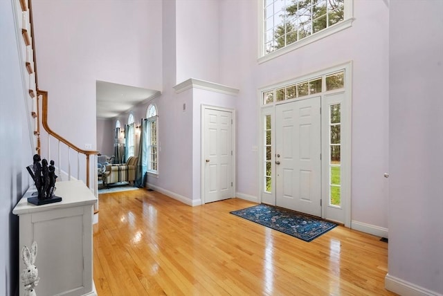 foyer entrance featuring baseboards, light wood-type flooring, a high ceiling, and stairs