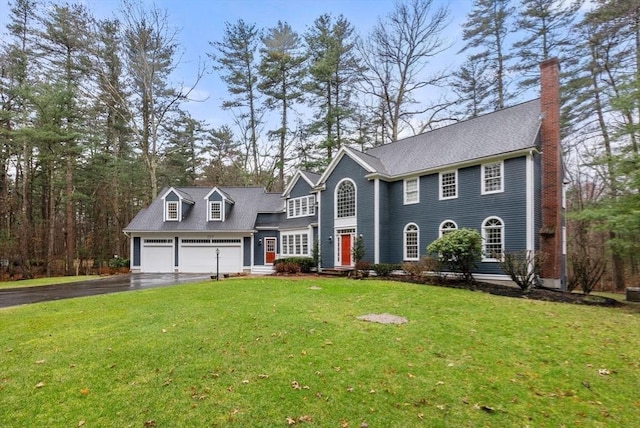 colonial home with a front lawn, a shingled roof, driveway, and a chimney