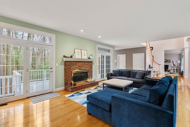 living room with visible vents, baseboards, a brick fireplace, stairway, and wood finished floors