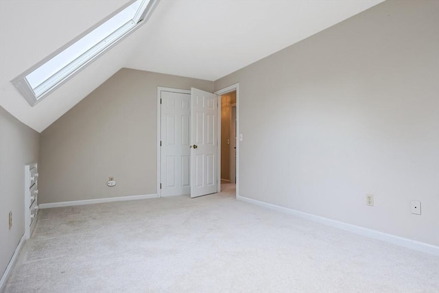 bonus room with vaulted ceiling with skylight, light colored carpet, and baseboards