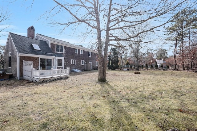 back of house featuring a chimney, a wooden deck, fence, and a shingled roof