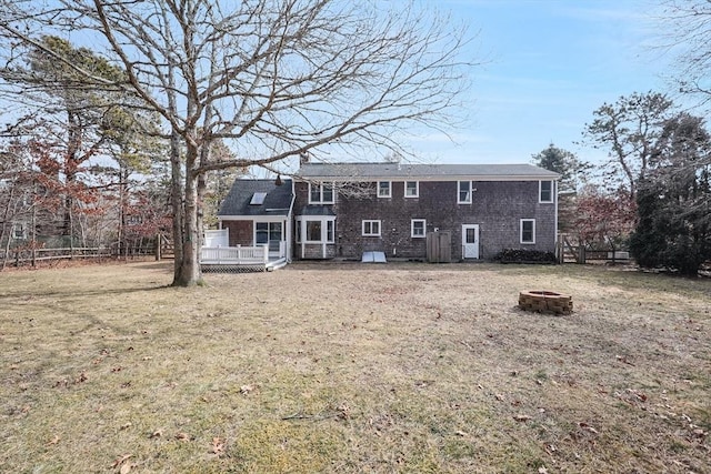 back of property featuring a wooden deck, a lawn, fence, and a fire pit